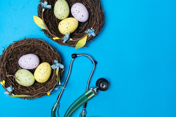 Easter Medicine. Two nests with painted eggs and a stethoscope on a blue background, space for text