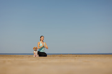 Fototapeta na wymiar woman and dog meditate on yoga mat on ocean in morning. sports outdoor for mental and physical health, breathing and physical practices. taking care of the body, spine and muscles