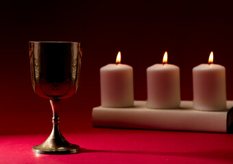 christian chalice on bible  by burning candles red background