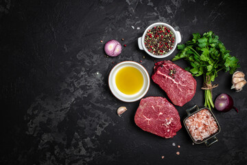 Two fresh raw beef steaks with spices ready to cook on a dark background. Culinary, cooking,...