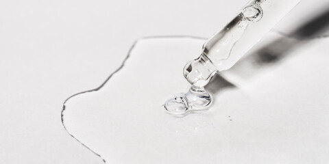 Drop of facial serum or oil with bubbles pouring from transparent pipette on grey background. Web...