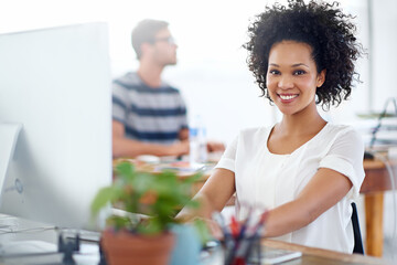 She makes a successful career look easy. Portrait of a smiling young designer working on a computer at a desk in an office.