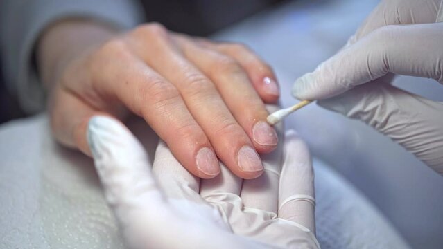 a person wearing disposable gloves rubs the oil into the nails