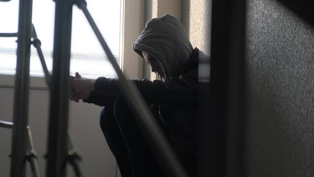 Thoughtful sad man in a hood thinks about something leaning against the wall
