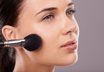 Blush with a brush. Studio shot of a beautiful young woman applying makeup to her face.