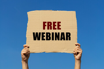 Free webinar text on box paper held by 2 hands with isolated blue sky background. This message board can be used as business concept about Free webinar.