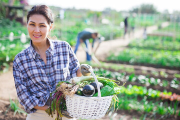 Portrait of female farmer with basket of vegetables on farm field