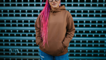 City portrait of handsome hipster girl with colored afro braids wearing brown blank hoodie or hoody with space for your logo or design. Mockup for print - obrazy, fototapety, plakaty