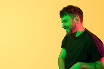 Creative portrait. Smiling man with closed eyes in green, pink neon lights on yellow background. Modern photo handsome bearded middle age man with earring in the ear. Copy space. Banner