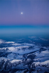 This photo taken from the plane shows the snow-covered Apennines with the moon in the background, creating a magical atmosphere. The mountain peaks appear as dark silhouettes against the night sky.