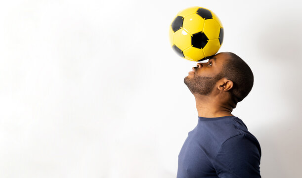 A dark-skinned man keeps a yellow soccer ball with his head on a white background. Soccer concept.