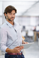 Hes a confident young businessman. Portrait of a handsome young businessman standing in his office holding a tablet.