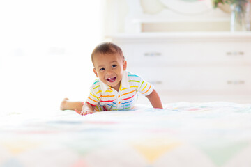 Baby boy playing on bed in sunny nursery