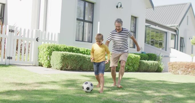 Happy caucasian grandfather and grandson playing football in garden, slow motion