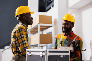 Two african american warehouse colleagues chatting at counter desk. Ecommerce store retail storehouse managers discussing customer order dispatching and standing near reception table