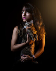 Mysterious Latina woman holding her gray cat in a low-key photo