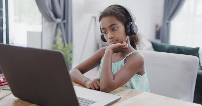 African american girl sitting at table, using laptop for online lesson, slow motion