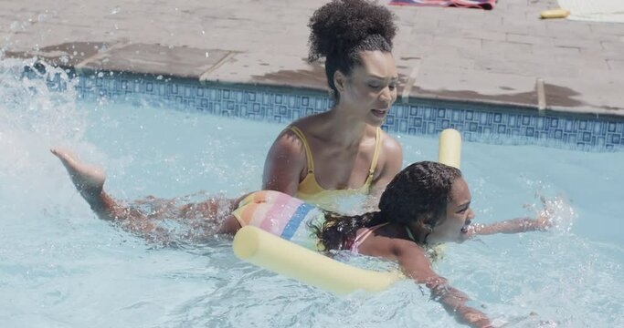 Happy african american mother and daughter having swimming lesson in swimming pool, slow motion
