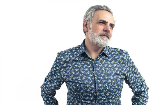 Studio Shot Of An Older Bearded Grey-haired Man In A Blue Patterned Button-up Shirt With Hands On His Waist. Serious Stance. Isolated On A White Background. High-quality Photo.