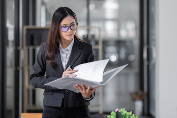 Portrait of cheerful young Asian business woman holding document folder and gets brilliant idea in mind office background