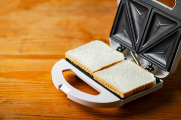 Sandwich maker with bread toast on wooden table. Preparation for preparation of sandwiches.
