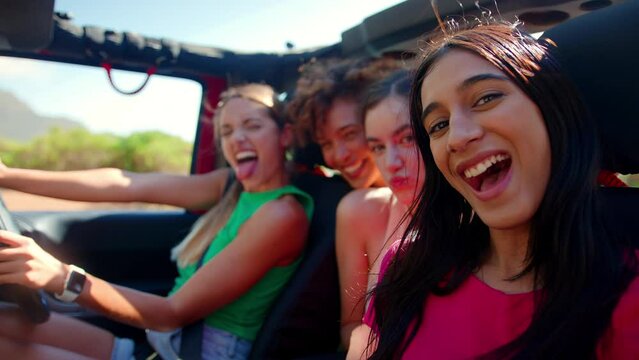 Portrait of female friends pulling faces in open top car laughing on road trip through countryside - shot in slow motion