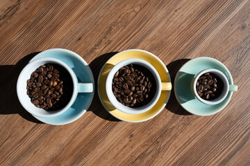 three cups with brown coffee beans on wooden table, top view