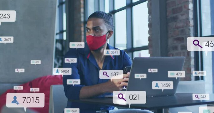 Animation of social media icons and numbers over biracial man in face mask using laptop