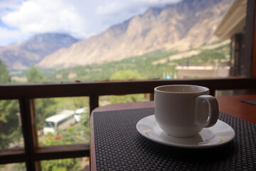 A beautiful view of Hunza valley from the window of a hotel, in the backdrop of a tea cup and saucer, represents the food, culture, and hospitality industry in Pakistan.