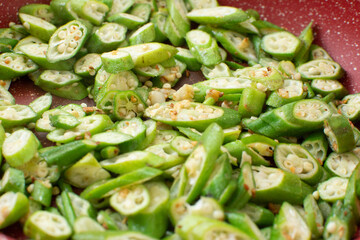 Close-up photo of sliced okra being fried in a red skillet