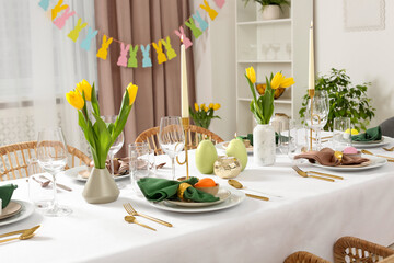 Festive Easter table setting with painted eggs, burning candles and yellow tulips in room
