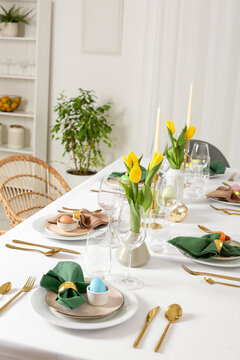 Festive Easter table setting with painted eggs, candles and yellow tulips in room
