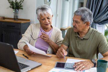 Biracial senior couple with calculator and bills analyzing finances and expenses on table at home