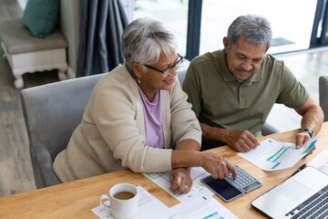 High angle view of biracial senior couple calculating expenses with bills on table at home