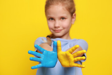 Little girl with hands painted in Ukrainian flag colors against yellow background, focus on palms. Love Ukraine concept