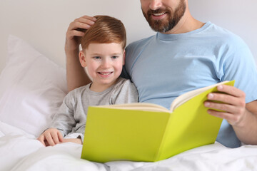 Father reading book with his child on bed at home