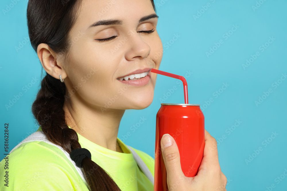 Wall mural Beautiful woman drinking from red beverage can on light blue background, closeup