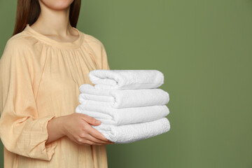 Woman holding folded soft terry towels on green background, closeup. Space for text