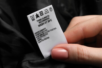 Woman holding clothing label on black garment, closeup