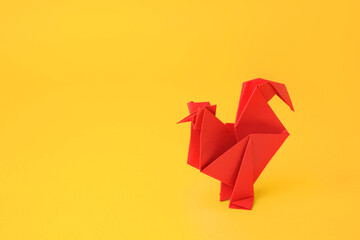 Origami art. Handmade red paper rooster on yellow background, space for text