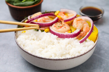 Delicious poke bowl with shrimps, rice and vegetables served on light grey table, closeup