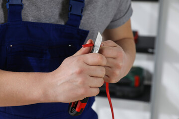 Professional electrician in uniform stripping wiring indoors, closeup