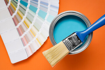 Can with light blue paint, brush and color palette on orange background, flat lay
