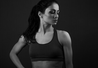 Fototapeta na wymiar Confident sportswoman in sportsbra, holding hands on waist, fitness trainer standing in power pose, workout in gym isolated on black background.