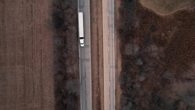 top down of a white Semi-trailer truck speeds on ramp enetering Interstate-highway I-94 Illinois. Tilting up and revealing horizon. Aerial 4k USA