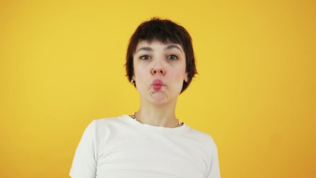 Surprised funny comical girl making fish face or doing duck grimace and laughing. Closeup shot over yellow background. Copy space. High quality 4k footage
