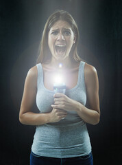 Horror movies have made her paranoid about the dark. A young brunette holding a flashlight while...