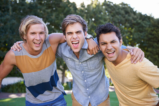 Friends for life. Portrait of three cheering friends standing with arms around each other in a park.