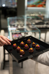 The waiter holds a Set of festive appetizer canapes on bread on a black tray as an event dish. Buffet table. Catering. Delicacy. Haute cuisine. 
