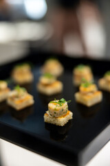 The waiter holds a Set of festive appetizer canapes on bread on a black tray as an event dish. Buffet table. Catering. Delicacy. Haute cuisine. 